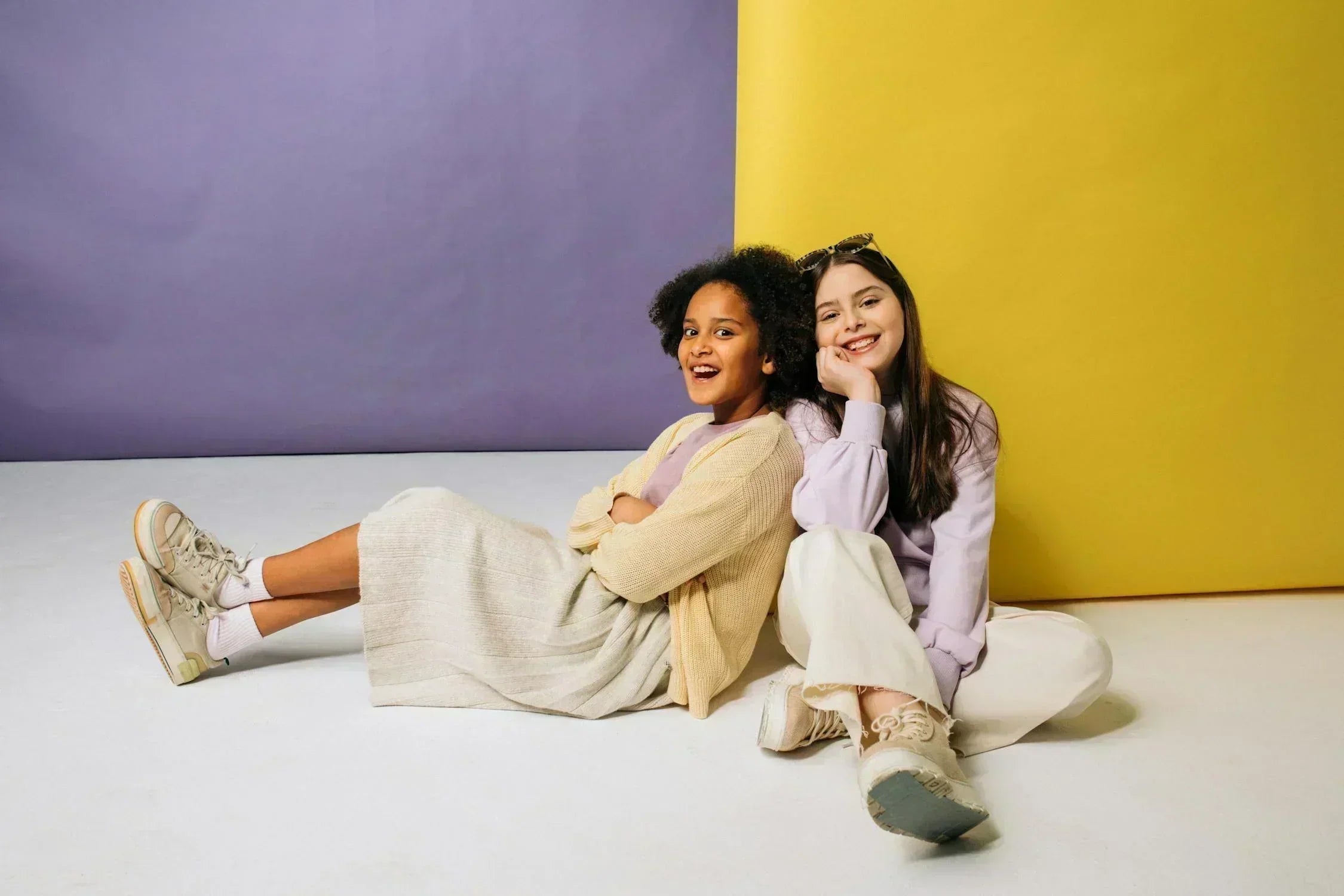 Two girls in pastel outfits pose against a colorful backdrop, highlighting trendy and comfy kids' Eid fashion for summer 2025.