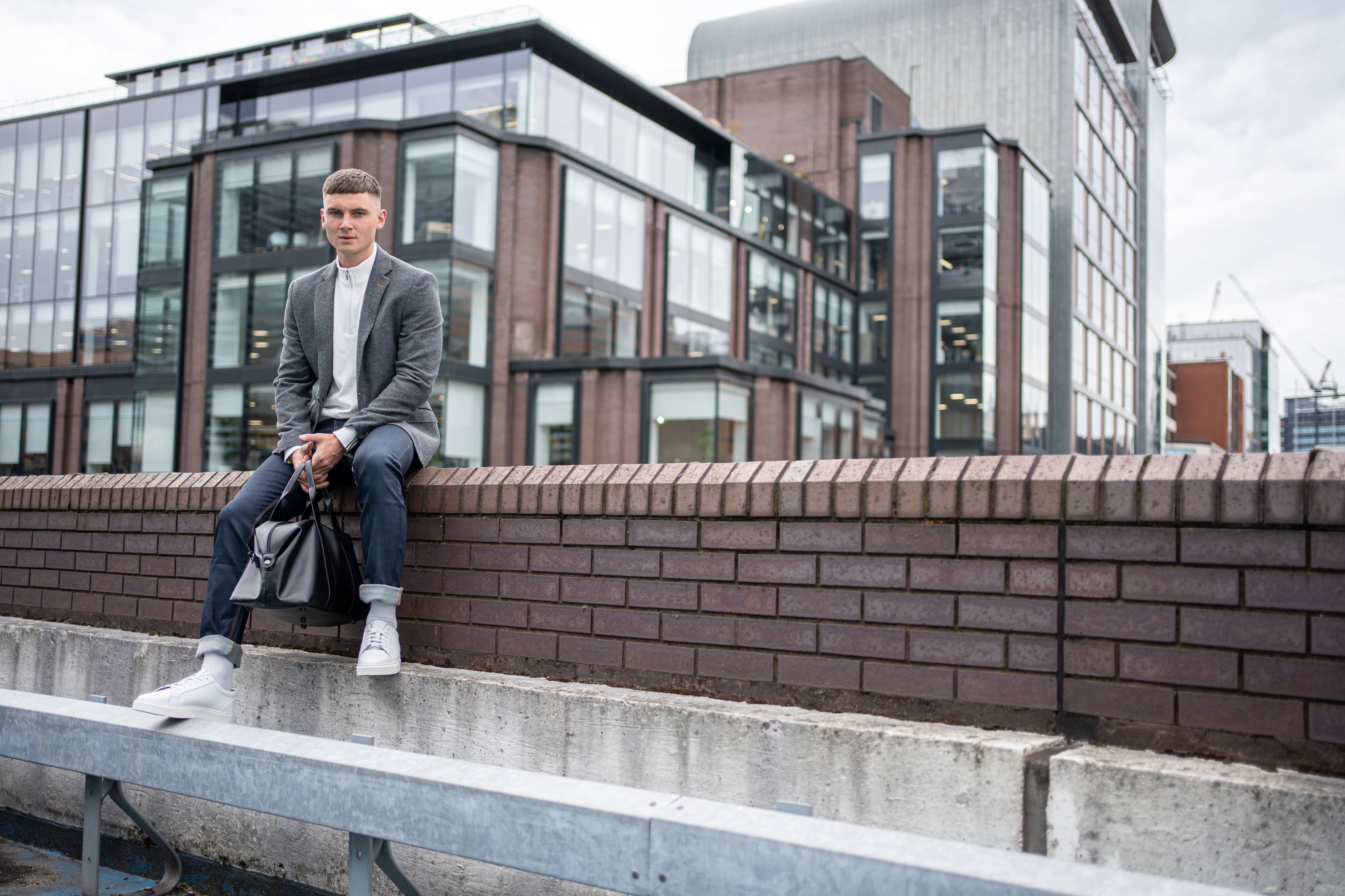 Man showcasing men's formalwear trends 2025 in a grey blazer, white shirt, and sneakers, blending tailored comfort with casual style.