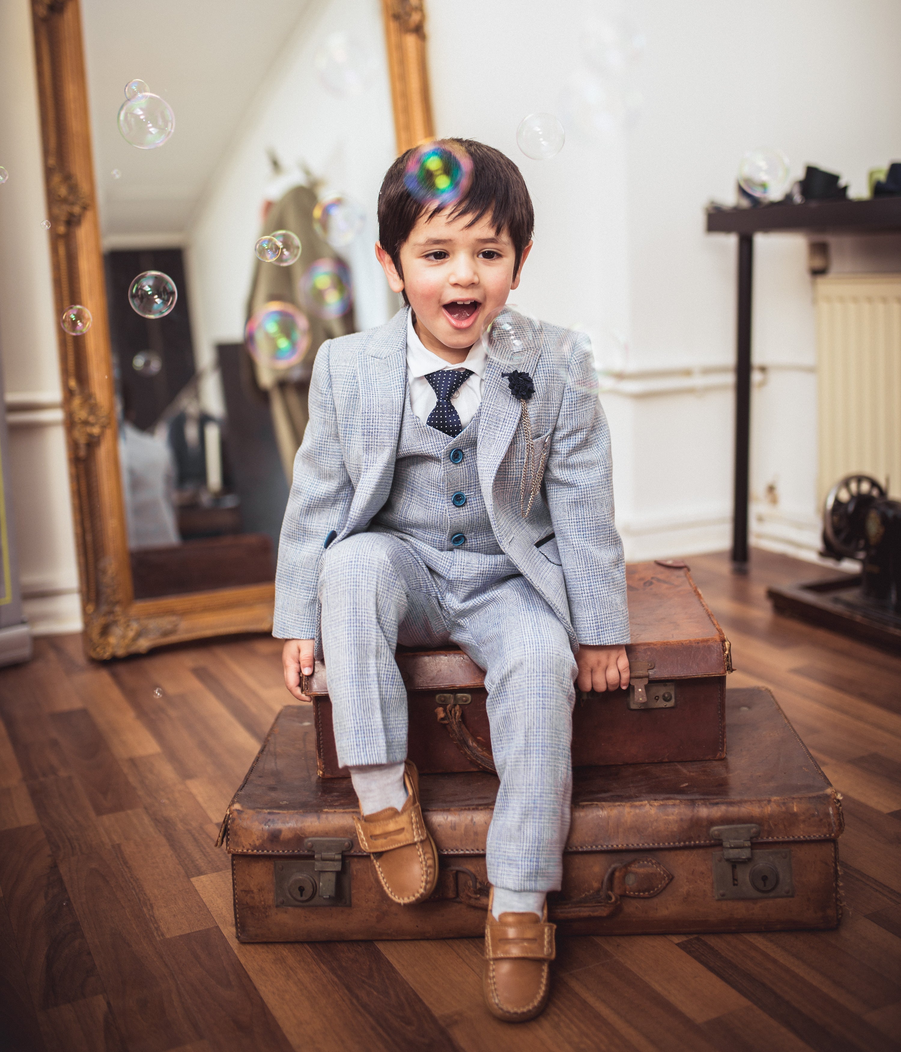 A young boy wearing a light blue page boy suit with navy accessories.